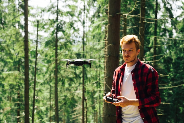 l'uomo con una maglietta rossa con un telecomando in mano controlla un drone in una bellissima foresta estiva