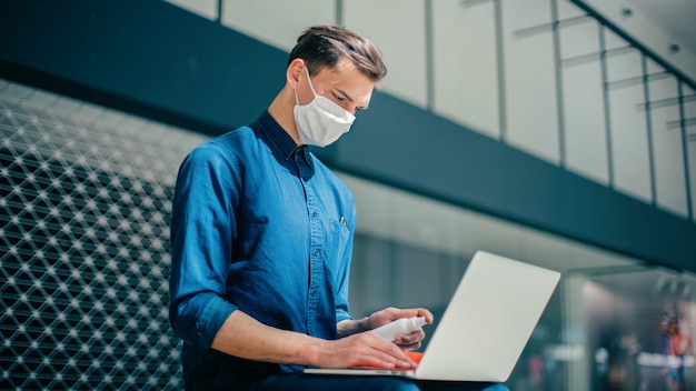L'uomo con una maschera protettiva disinfetta il suo laptop. pandemia in città
