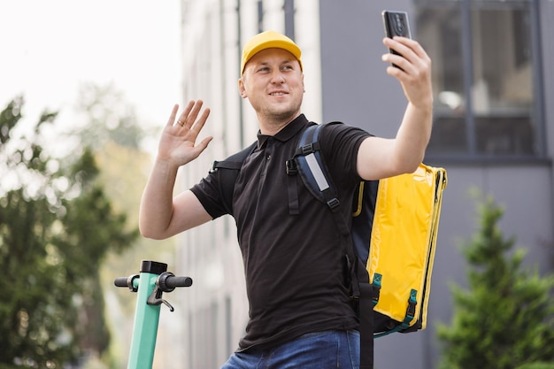 L'uomo consegna cibo corriere con zaino termico giallo cammina per strada con scooter elettrico