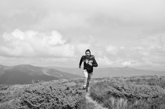 L'uomo corre sul prato verde in montagna sul cielo nuvoloso