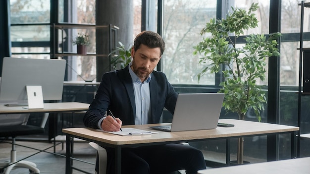 L'uomo d'affari adulto concentrato lavora sul progetto in ufficio usando il computer portatile che scrive le note uomo caucasico