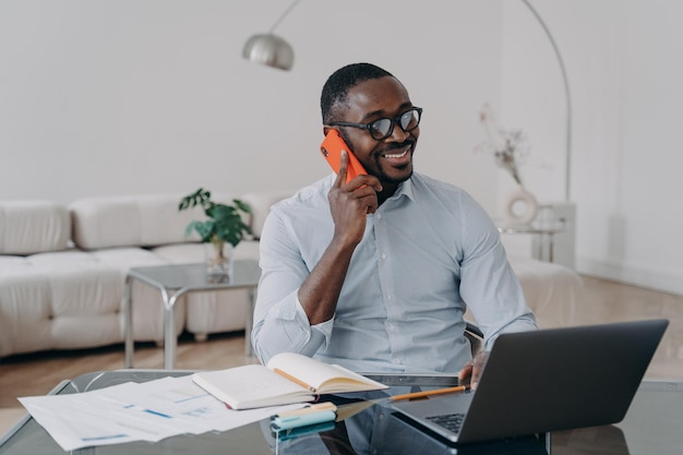 L'uomo d'affari afroamericano effettua telefonate di lavoro godendo di una conversazione mobile lavora al computer portatile
