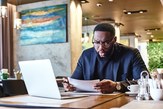 L'uomo d'affari afroamericano sta lavorando usando il suo computer portatile mentre riposa nel caffè