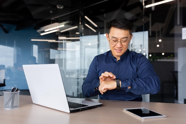 L'uomo d'affari asiatico di successo usa l'orologio intelligente sul posto di lavoro l'uomo sceglie le app e sorride felice con le app