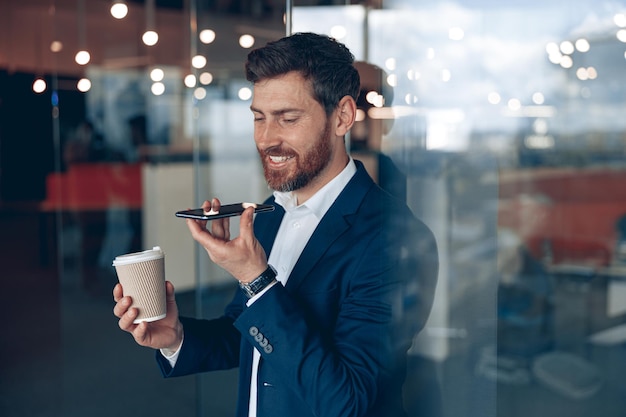 L'uomo d'affari bello sta usando lo smartphone per registrare un messaggio vocale al partner commerciale