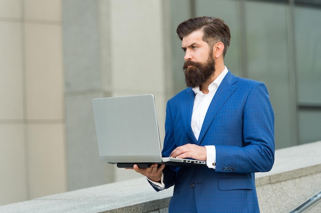 L'uomo d'affari brutale in completo formale usa il laptop per lavorare online all'aperto, e-business.