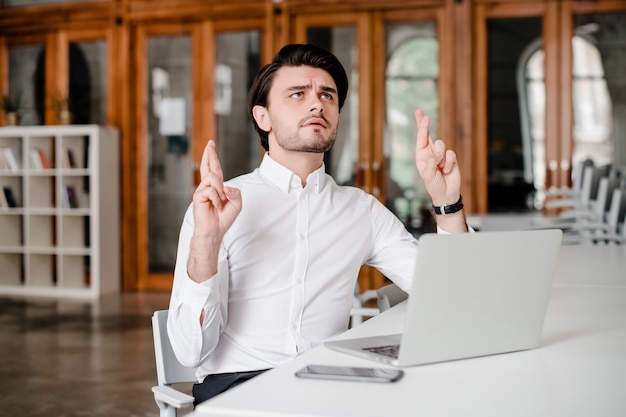 L'uomo d'affari che spera e che prega le dita della tenuta ha attraversato nell'ufficio