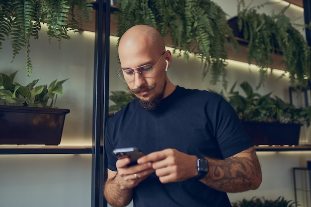 L'uomo d'affari concentrato utilizza lo smartphone con le cuffie mentre si trova nel lavoro a distanza dell'ufficio domestico