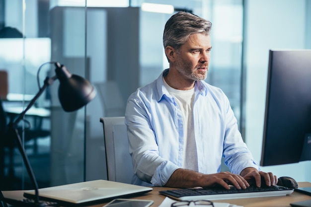 L'uomo d'affari dai capelli grigi con esperienza lavora al computer in un ufficio moderno