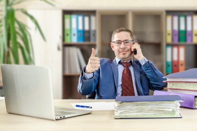 L'uomo d'affari del capo mostra il gesto del segno del pollice in su Parlando al telefono Desktop in ufficio