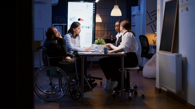 L'uomo d'affari disabile oberato di lavoro in sedia a rotelle viene ignorato mentre lavora nella sala riunioni dell'ufficio aziendale a tarda notte