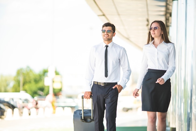 L'uomo d'affari e la donna con gli occhiali da sole camminano con una valigia