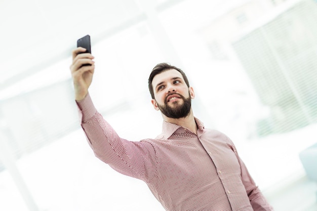 L'uomo d'affari fa selfie stando in piedi vicino alla finestra in ufficio