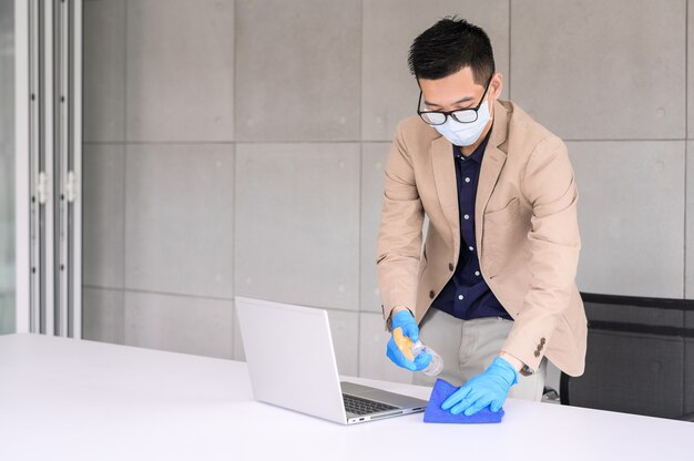 L'uomo d'affari facendo uso del panno del microfiber e del disinfettante dell'alcool spruzzano per pulire il computer portatile e la tavola