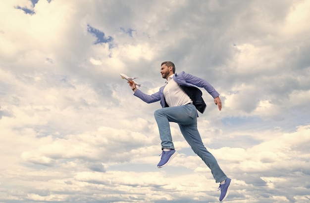 L'uomo d'affari felice in giacca tiene l'aereo giocattolo sullo sfondo del cielo per raggiungere il successo