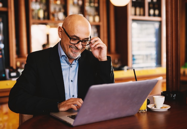 L'uomo d'affari felice maturo sta sedendosi in una caffetteria e sta navigando su Internet.