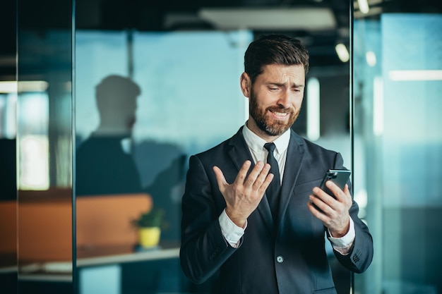 L'uomo d'affari frustrato che guarda al telefono l'uomo ha ricevuto cattive notizie mentre lavorava in un ufficio moderno