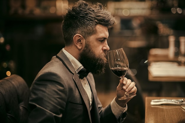 L'uomo d'affari perfetto del vino con la bevanda lunga della barba nel cliente del bar del sigaro si siede nella caffetteria che beve alcol