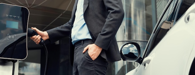 L'uomo d'affari progressivo del primo piano inserisce la spina del caricatore dalla stazione di ricarica al veicolo elettrico