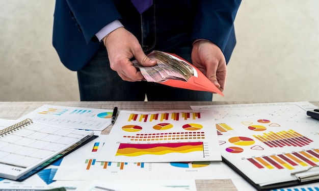 L'uomo d'affari riceve un reddito nascosto in una busta dall'azienda. Un uomo lavora con un programma di lavoro e mantiene un profitto in ufficio. Il concetto di paga o corruzione.