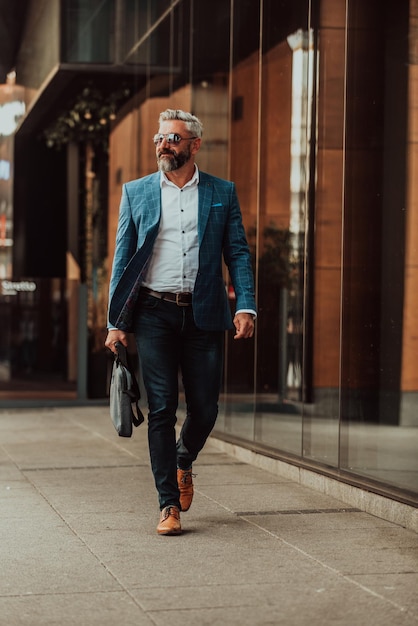 L'uomo d'affari senior moderno con una borsa esce dalla società moderna.