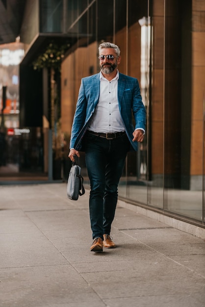 L'uomo d'affari senior moderno con una borsa esce dalla società moderna.