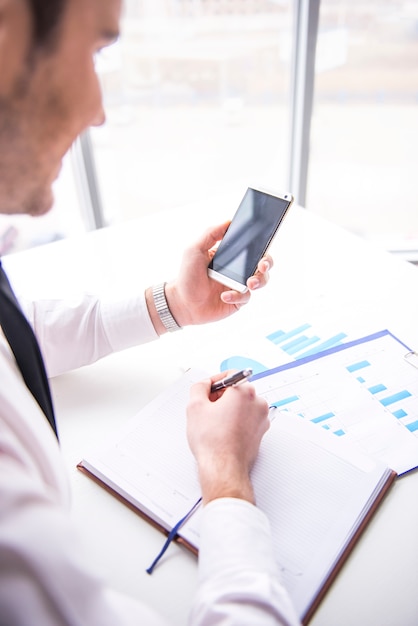 L'uomo d'affari sta utilizzando il telefono cellulare allo scrittorio in ufficio.