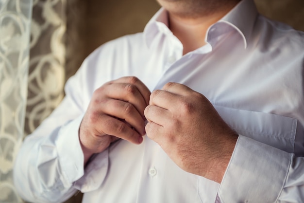 L'uomo d'affari veste la camicia bianca, il primo piano delle mani maschile, lo sposo si prepara al mattino prima della cerimonia nuziale,