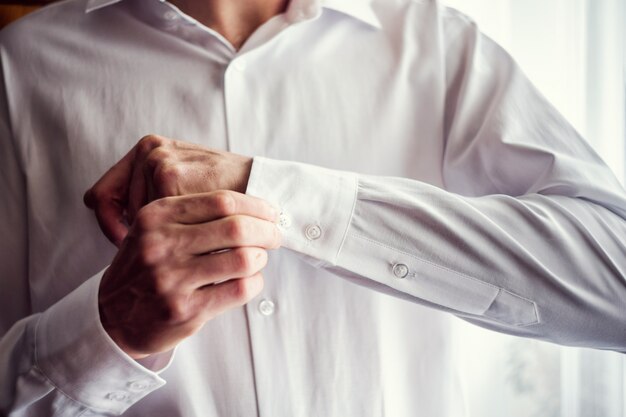 L'uomo d'affari veste la camicia bianca, il primo piano delle mani maschile, lo sposo si prepara al mattino prima della cerimonia nuziale,