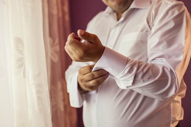 L'uomo d'affari veste la camicia bianca, il primo piano delle mani maschile, lo sposo si prepara al mattino prima della cerimonia nuziale,