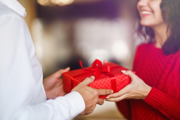 L'uomo dà alla sua donna una confezione regalo con nastro rosso Le mani dell'uomo regalano una confezione regalo a sorpresa per la ragazza