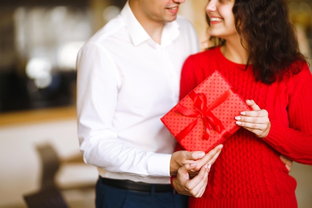 L'uomo dà alla sua donna una confezione regalo con nastro rosso Le mani dell'uomo regalano una confezione regalo a sorpresa per la ragazza