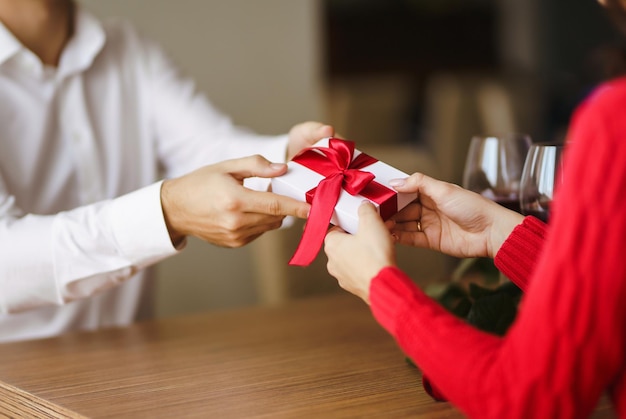 L'uomo dà alla sua donna una confezione regalo con nastro rosso Le mani dell'uomo regalano una confezione regalo a sorpresa per la ragazza