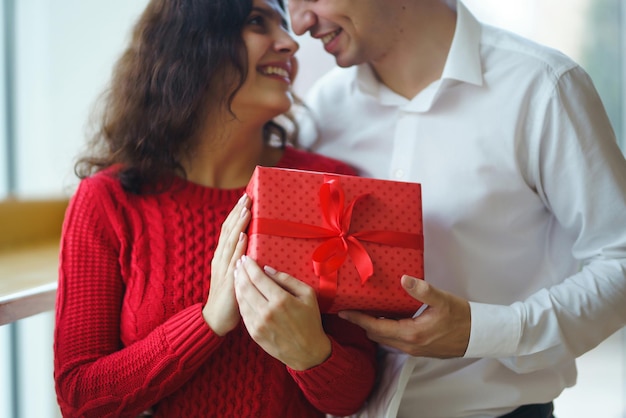 L'uomo dà alla sua donna una confezione regalo con nastro rosso Una coppia di innamorati coccole e festeggia San Valentino