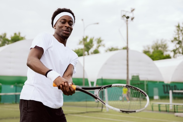 L'uomo dall'aspetto africano gioca a tennis sul campo da tennis, tiene in mano la racchetta e colpisce la palla