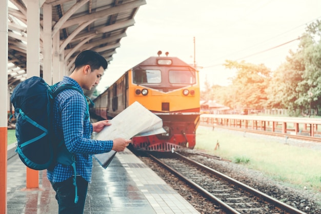 L&#39;uomo del viaggiatore con la mappa e aspetta il treno sulla piattaforma ferroviaria