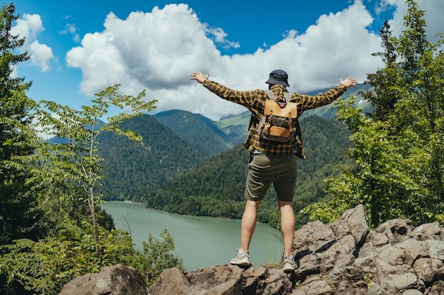 L'uomo del viaggiatore escursionistico con lo zaino alza le mani godendo della splendida vista del lago Ritsa in Abkhazia