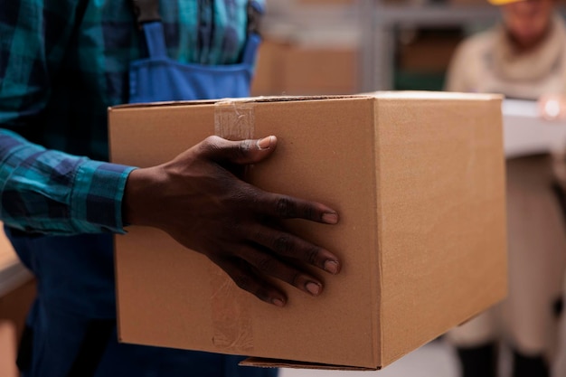 L'uomo dell'operaio del magazzino dell'afroamericano passa la tenuta del pacchetto del cartone. Le braccia dei dipendenti del magazzino che trasportano un contenitore di cartone con nastro adesivo si chiudono, lavorando in magazzino