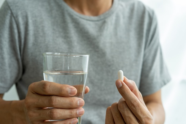 L'uomo della mano che tiene un integratore alimentare o un farmaco o una vitamina e un bicchiere d'acqua pronto da prendere. sanità, medicina, cura di sé, malattia e concetto di farmacia.