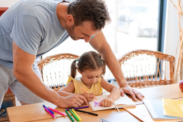 L'uomo della tata è impegnato in un lavoro creativo con una bambina, osservando come disegna con pennarelli colorati su un quaderno.