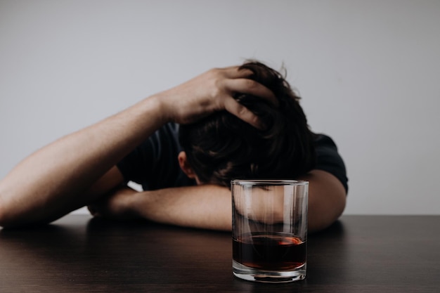 L'uomo depresso dell'alcolismo dorme sul tavolo mentre beve una bevanda alcolica con un bicchiere di whisky
