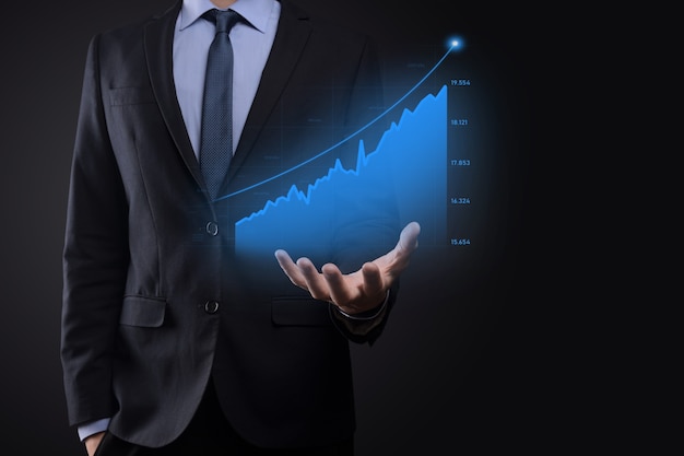 L'uomo di affari che tiene i grafici olografici e le statistiche del mercato azionario guadagna i profitti