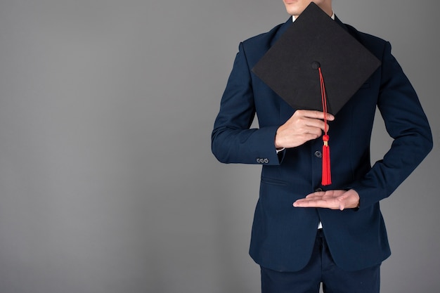 L&#39;uomo di affari sta tenendo il cappello di graduazione, concetto di istruzione di affari