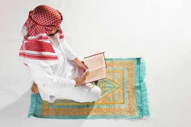 L'uomo di alta vista che si siede sul tappeto di preghiera e legge