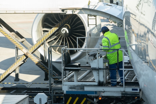 L&#39;uomo di carico sulla piattaforma di carico carica il trasporto aereo verso gli aerei cargo.