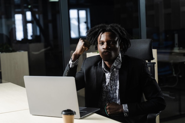 L'uomo di colore felice ha stretto i pugni e si è rallegrato di finire il suo lavoro online sul laptop. Lavorare online nello spazio di coworking.