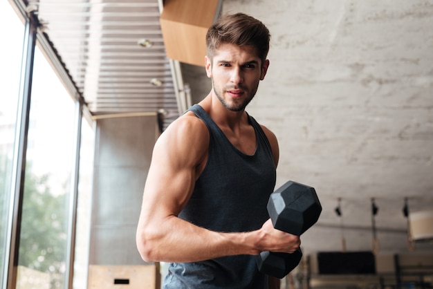 L'uomo di forma fisica sta lateralmente in palestra. guardando davanti. con manubri