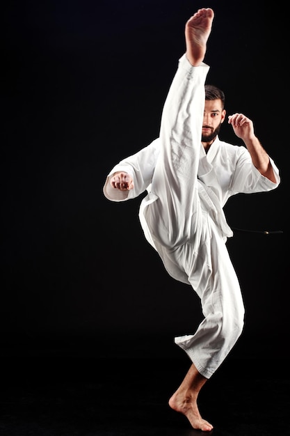 L'uomo di karate in kimono colpisce il piede su sfondo nero