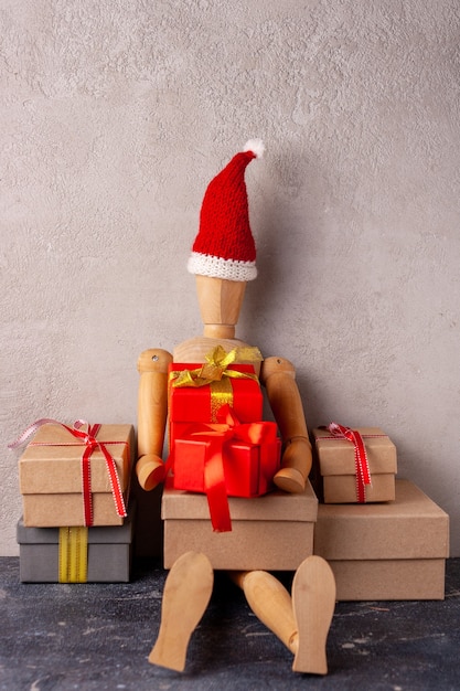 L'uomo di legno con un cappello da Babbo Natale siede accanto a una montagna di regali