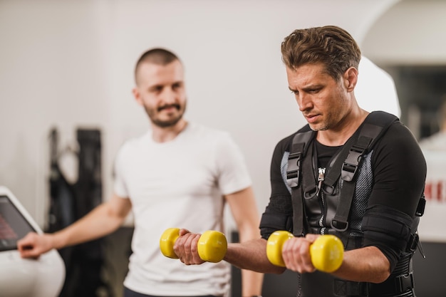 L'uomo di mezza età sta facendo EMS che si allena con il personal trainer in palestra.